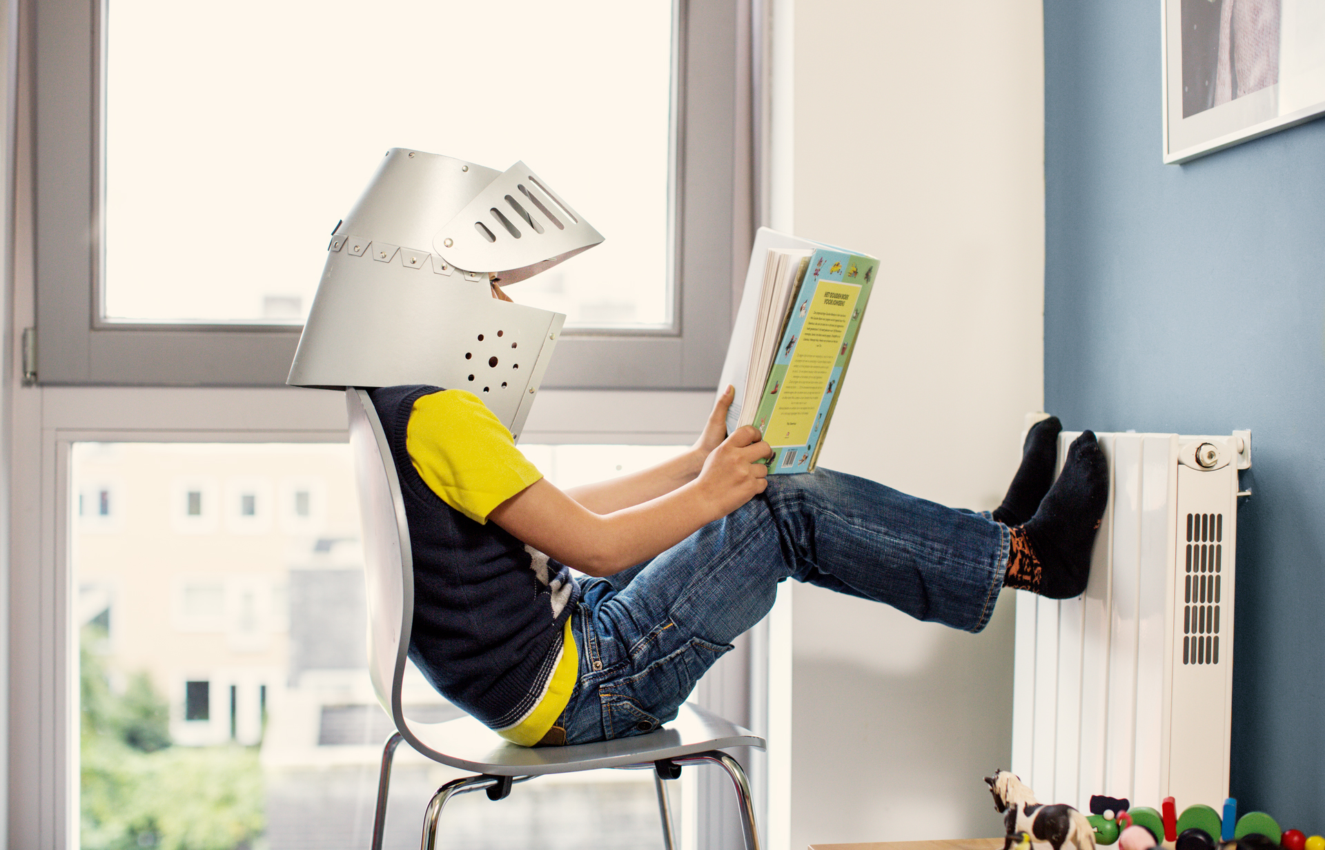 Junge sitzt am Heizkörper und liest ein Buch.