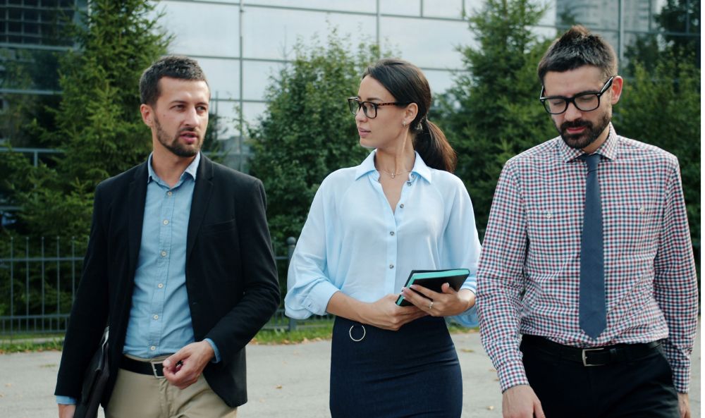 KI-Kompetenz und KI-Verordnung: Das Foto zeigt drei Menschen, die in einem Büro und einen Tisch herum sitzen und arbeiten