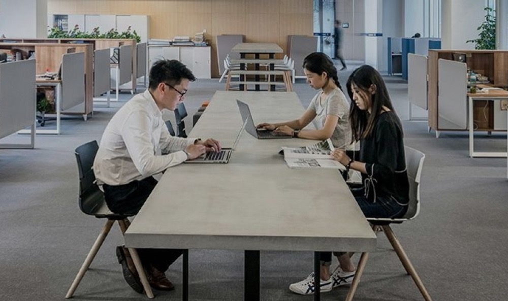 KI-Kompetenz und KI-Verordnung: Das Foto zeigt drei Menschen, die in einem Büro und einen Tisch herum sitzen und arbeiten