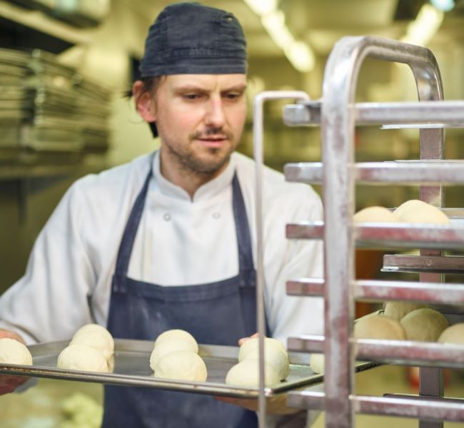 Bild zum Thema Best Practice Mittelstand Image und Zielgruppe - zu sehen ist ein Koch des Restaurants TRUDE in Hamburg, der gerade selbstgemachten Teig auf Blechen trägt - Ein Bild für den Artikel "Was bedeutet Nachhaltigkeit für Unternehmen"