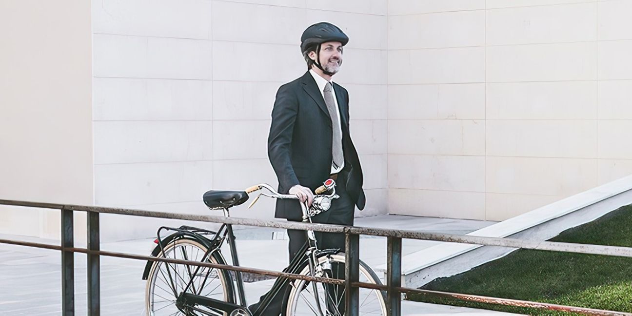 Mann im Businessanzug und Sturzhelm schiebt sein Dienstfahrrad