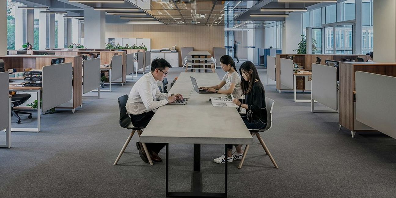 Ein Foto von drei Menschen, die in einem Großraumbüro gemeinsam an einem Tisch arbeiten
