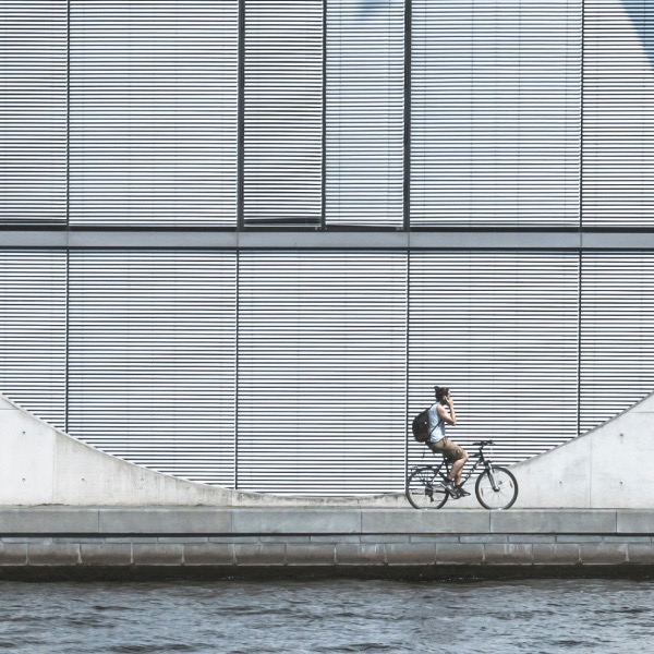 Dienstfahrrad: Eine telefonierende Frau fährt vor einem minimalistischen Hintergrund