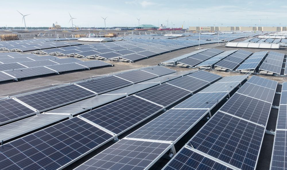 Dieses Bild zeigt Solarflächen, die auf einem Dach aufgebaut werden und Windräder in der Ferne.