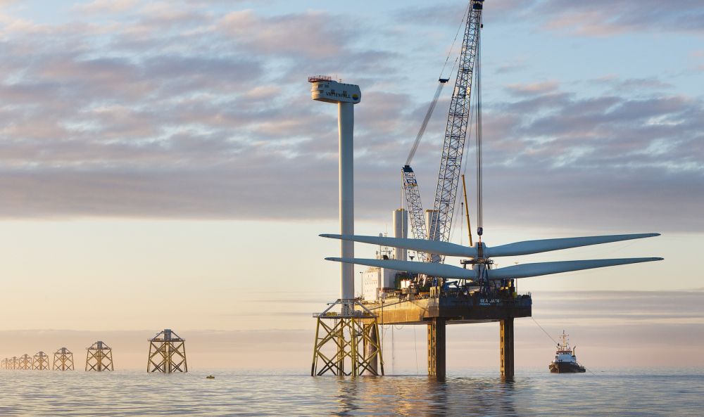 Dieses Bild zeigt Solarflächen, die auf einem Dach aufgebaut werden und Windräder in der Ferne.