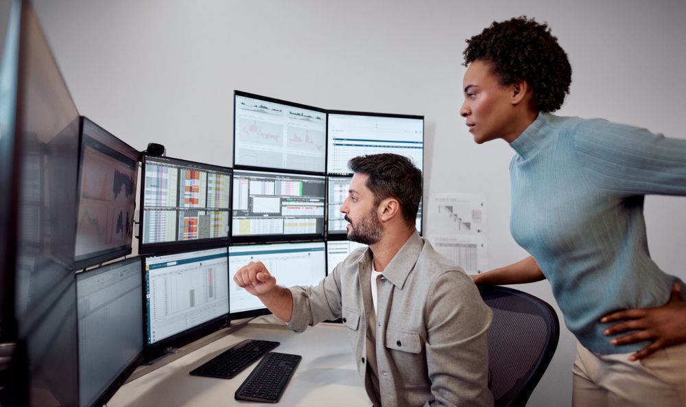 Zwei Menschen am Arbeitsplatzen vor Bildschirmen verdeutlichen das Thema Strompreisentwicklung 2025
