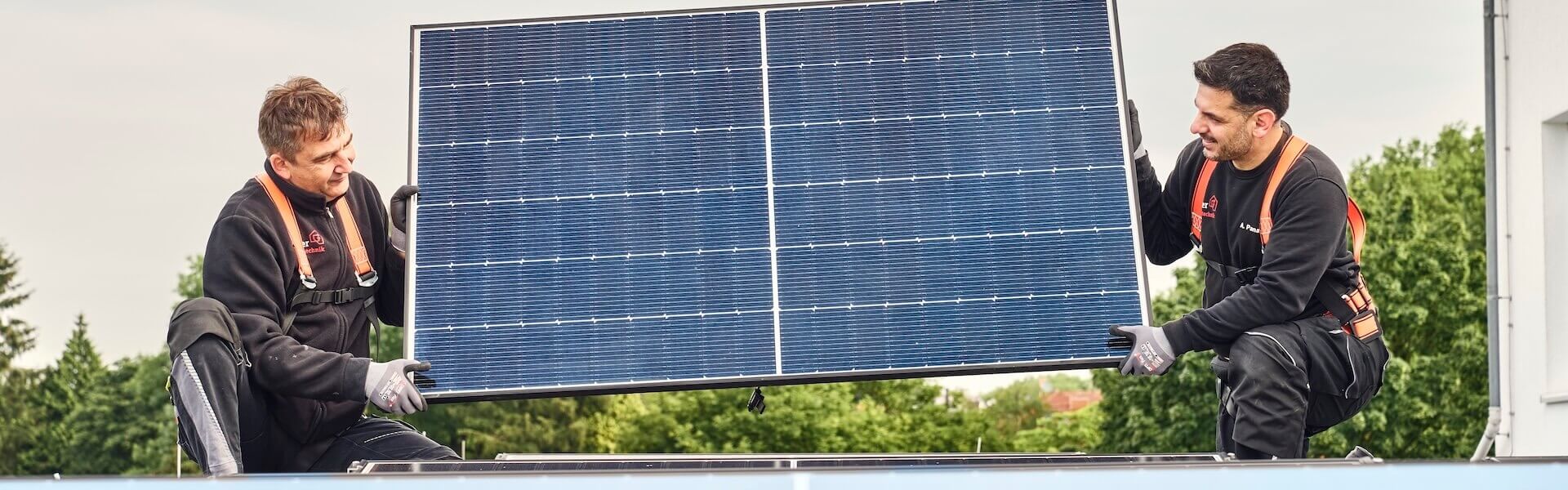 Zwei Männer tragen ein Solarpaneel, um es zu montieren.