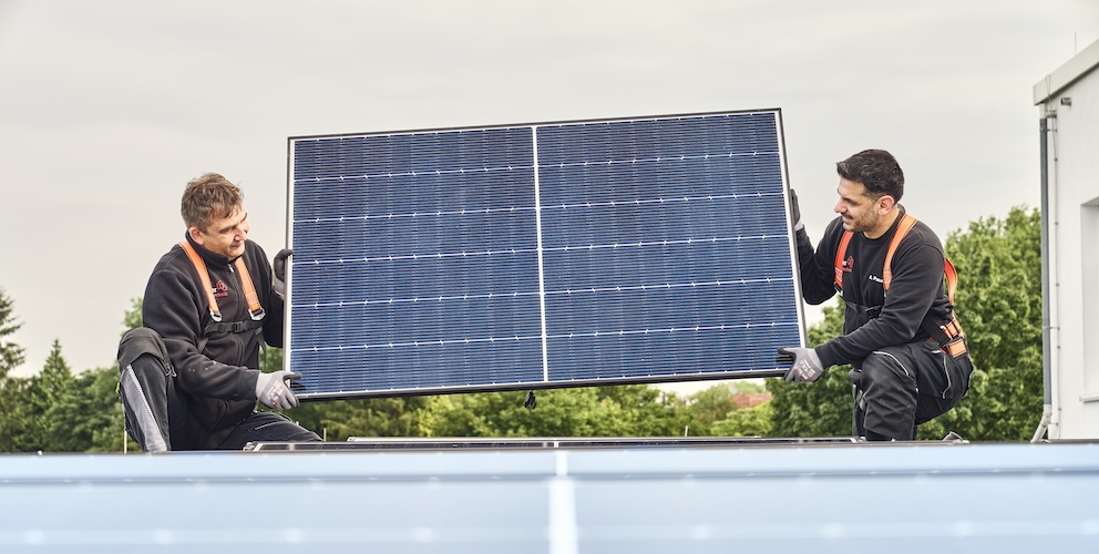 Zwei Männer tragen ein Solarpaneel, um es zu montieren.