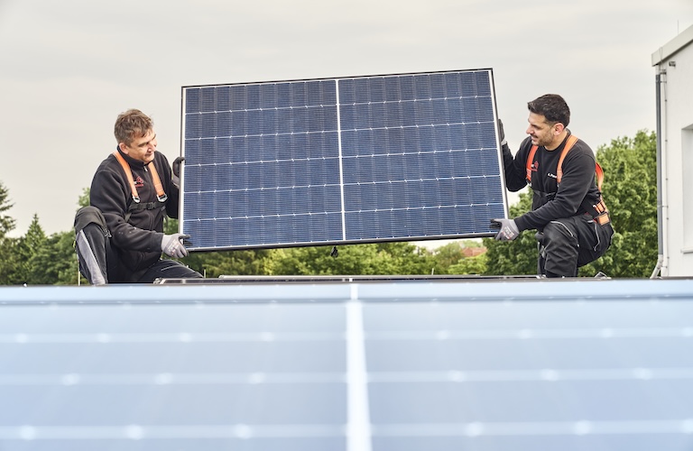 Zwei Männer tragen ein Solarpaneel, um es zu montieren.