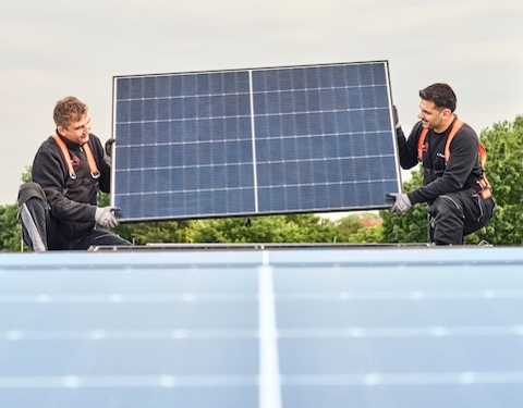 Zwei Männer tragen ein Solarpaneel, um es zu montieren.