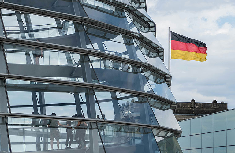 Ein Ausschnitt der Reichstagskuppel ist sichtbar. Dahinter weht eine Deutschlandfahne.