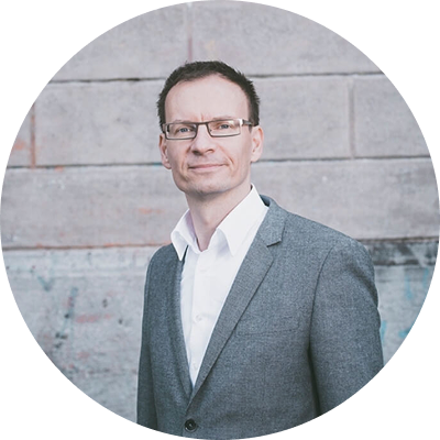 Mann in Anzug steht vor grauer Wand.