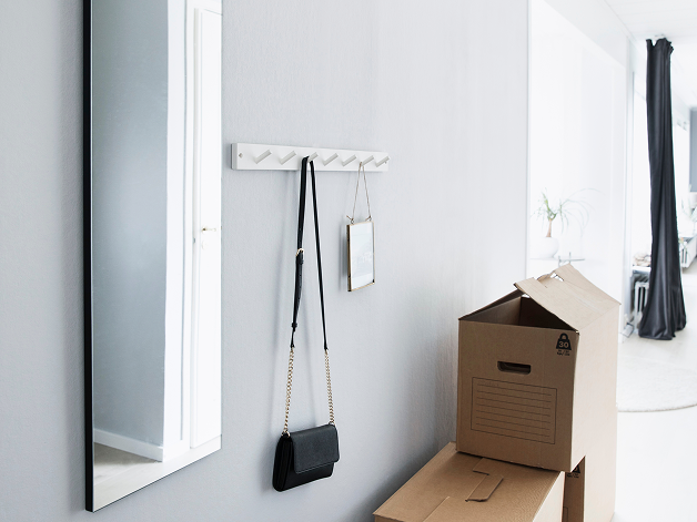 Heller Flur mit Wandspiegel, Hakenleiste mit Schlüsseln und offenem Karton.