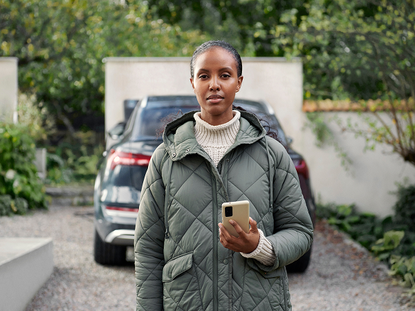Frau steht mit einem Handy in der Hand vor einem Auto