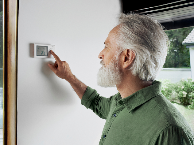 Älterer Mann stellt ein Thermostat an einer weißen Wand ein.