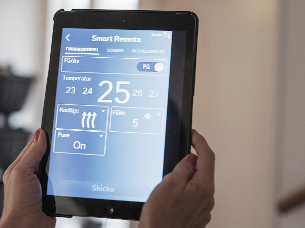 Hände halten ein Tablet mit geöffneter Smart-Home-Steuerung; auf dem Display sind Grundriss und vernetzte Geräte zu sehen – Hausautomation im Einsatz.
