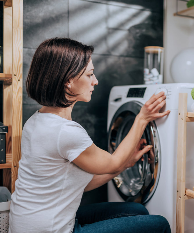 Frau schaltet einen Wäschetrockner ein.