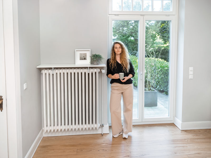 Frau steht mit Tasse an Heizkörper