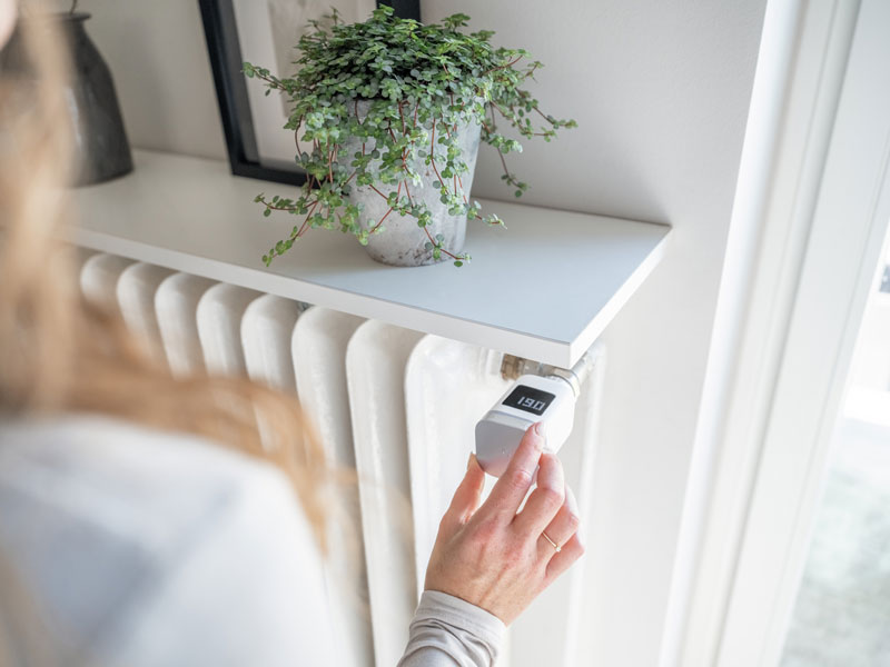 Frau am Heizkörper mit programmierbarem Thermostat