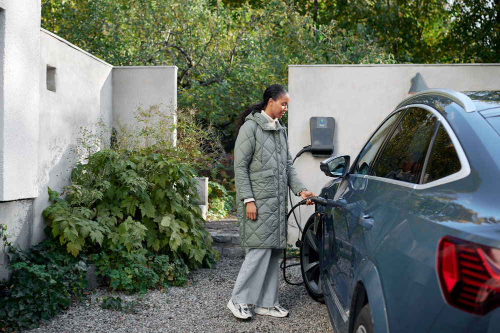 Frau steht an ihrem E-Auto, das gerade lädt