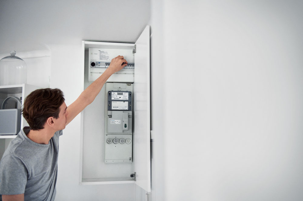 Mann steht am geöffneten Sicherungskasten