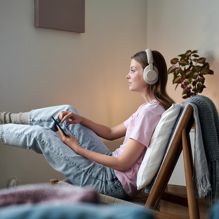 Frau auf Stuhl trägt Over-Ear Bluetooth Kopfhörer