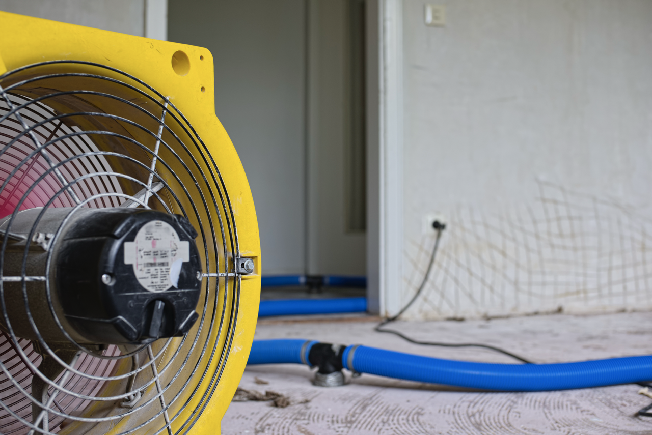 Lüfter und blaue Schläuche zur Trocknung nach Wasserschaden in einem Innenraum.