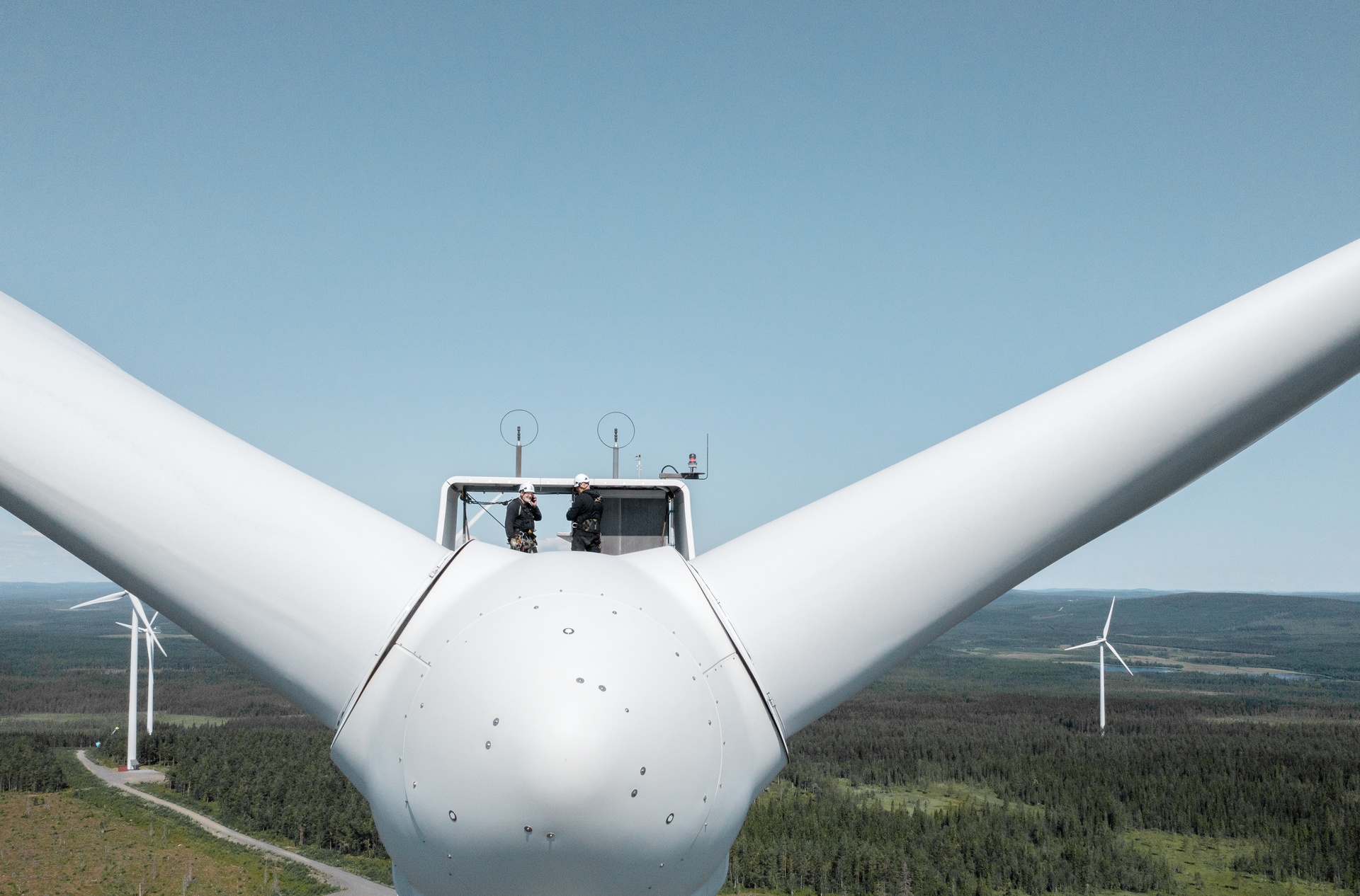 Zwei Arbeiter stehen in luftiger Höher auf der Verbindungsstelle der Rotorblätter einer Windanlage.