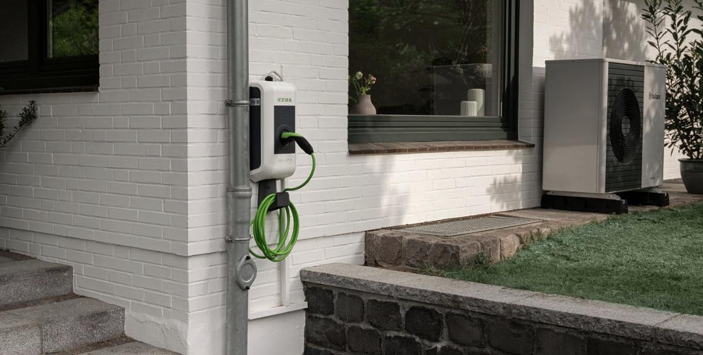 KEBA-Wallbox an einer Hauswand eines Einfamilienhauses. Im Hintergrund steht eine Wärmepumpe.