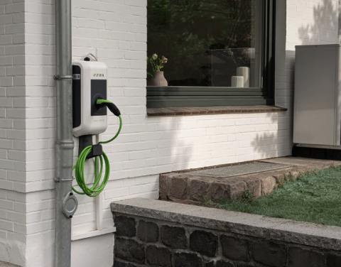 KEBA-Wallbox an einer Hauswand eines Einfamilienhauses. Im Hintergrund steht eine Wärmepumpe.