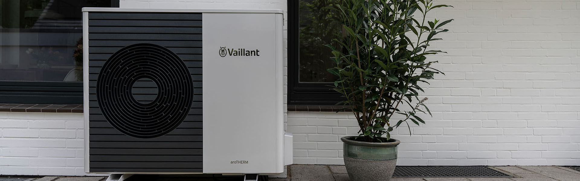 Eine Vaillant Wärmepumpe steht an einer Hauswand, daneben befindet sich eine Topfpflanze.