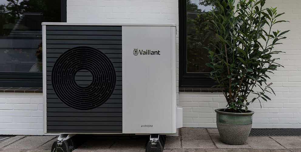 Eine Vaillant Wärmepumpe steht an einer Hauswand, daneben befindet sich eine Topfpflanze.