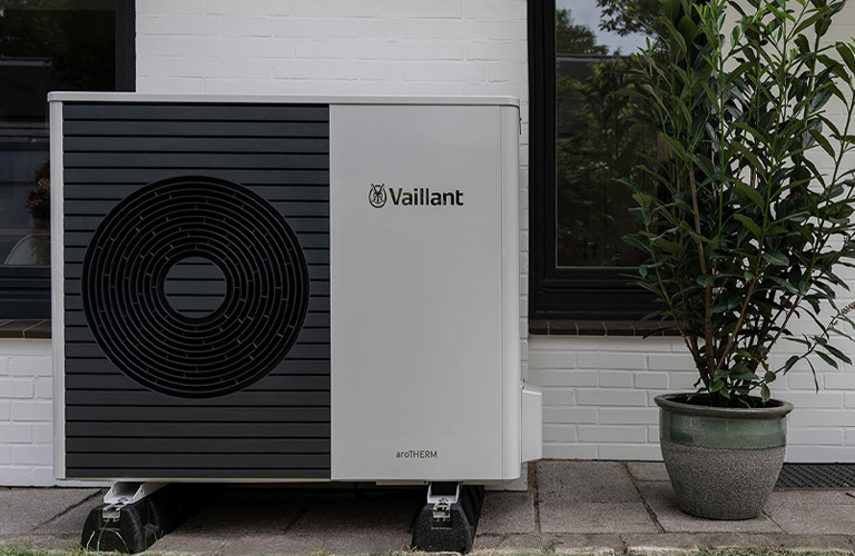 Eine Vaillant Wärmepumpe steht an einer Hauswand, daneben befindet sich eine Topfpflanze.