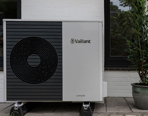 Eine Vaillant Wärmepumpe steht an einer Hauswand, daneben befindet sich eine Topfpflanze.