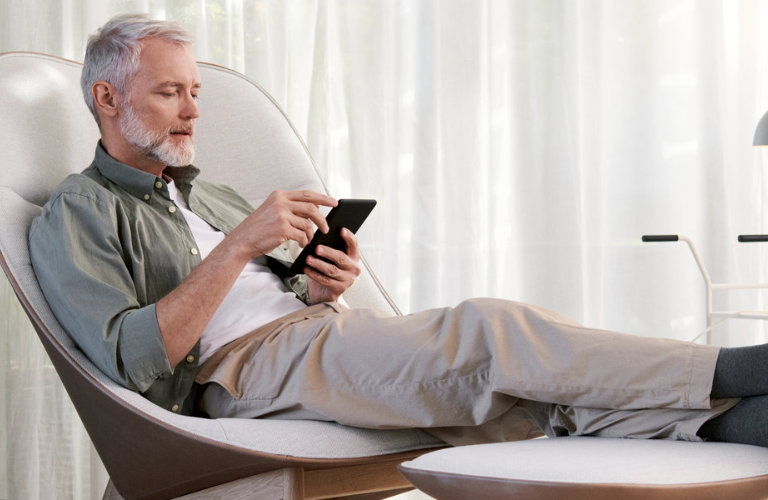 Mann sitzt im Wohnzimmer auf einem Sessel und schaut auf sein Smartphone.