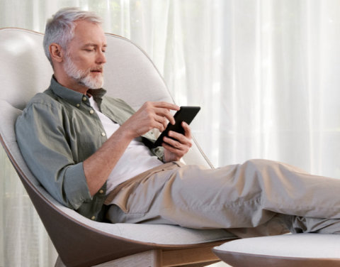 Mann sitzt im Wohnzimmer auf einem Sessel und schaut auf sein Smartphone.