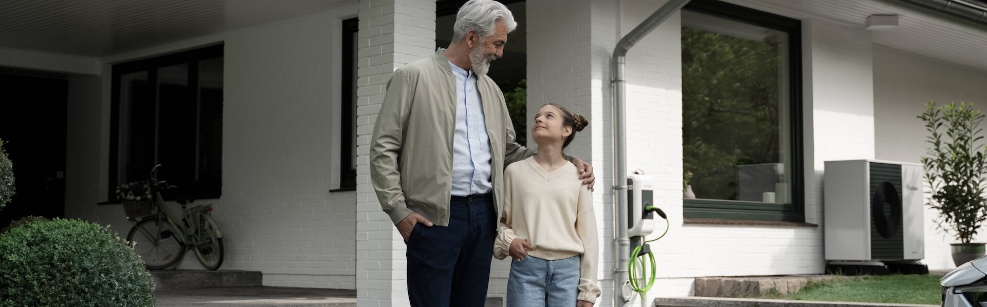 Älterer Mann umarmt Kind vor Einfamilienhaus.