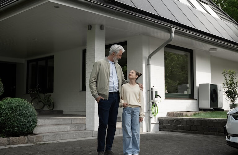 Älterer Mann umarmt Kind vor Einfamilienhaus.