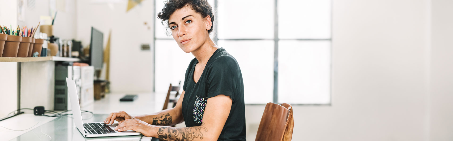 Frau sitzt am Schreibtisch und arbeitet am Laptop.