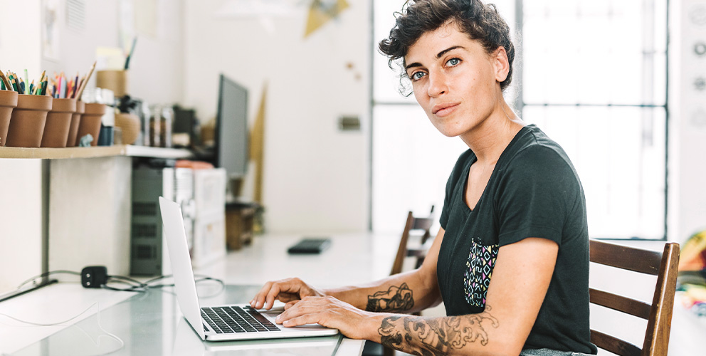 Frau sitzt am Schreibtisch und arbeitet am Laptop.