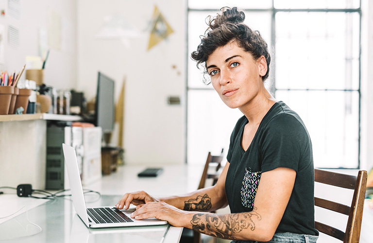 Frau sitzt am Schreibtisch und arbeitet am Laptop.
