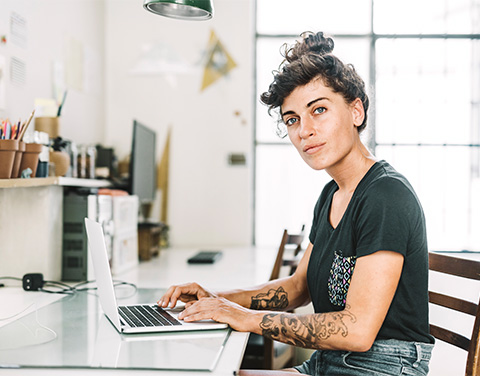 Frau sitzt am Schreibtisch und arbeitet am Laptop.