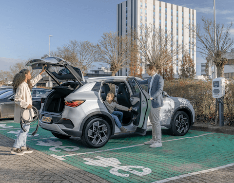 Familie parkt mit E-Auto auf Parkplatz.