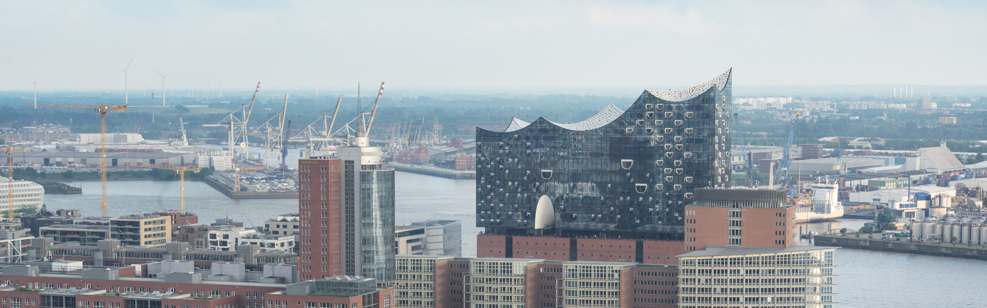 Blick über die Skyline von Hamburg mit der Elbphilharmonie  im Vordergrund und dem Hafen dahinter.