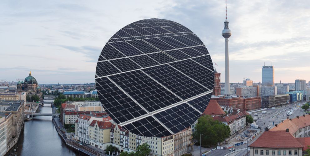 Blick über die Skyline von Berlin mit Sicht auf die Spree und den Fernsehturm. Im Vordergrund eine Nahaufnahme einer Photovoltaikanlage.