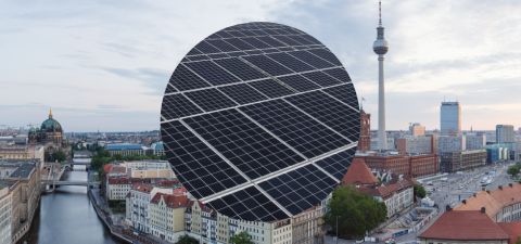 Blick über die Skyline von Berlin mit Sicht auf die Spree und den Fernsehturm. Im Vordergrund eine Nahaufnahme einer Photovoltaikanlage.