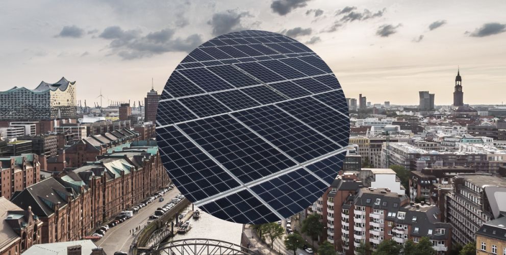 Blick über die Skyline von Hamburg mit Sicht auf die Speicherstadt. Im Hintergrund sind die Michaeliskirche und die Elbphilharmonie zu sehen. Im Vordergrund eine Nahaufnahme einer Photovoltaikanlage.