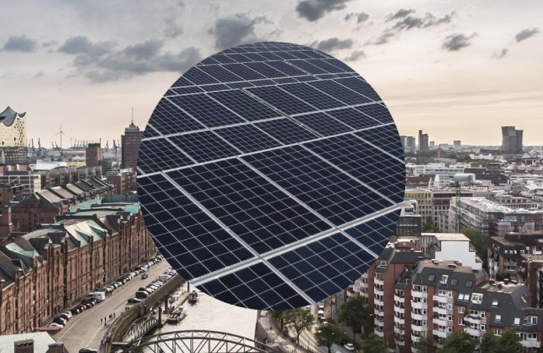 Blick über die Skyline von Hamburg mit Sicht auf die Speicherstadt. Im Hintergrund sind die Michaeliskirche und die Elbphilharmonie zu sehen. Im Vordergrund eine Nahaufnahme einer Photovoltaikanlage.