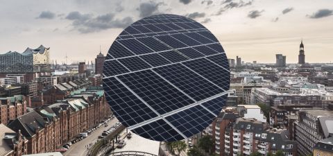 Blick über die Skyline von Hamburg mit Sicht auf die Speicherstadt. Im Hintergrund sind die Michaeliskirche und die Elbphilharmonie zu sehen. Im Vordergrund eine Nahaufnahme einer Photovoltaikanlage.