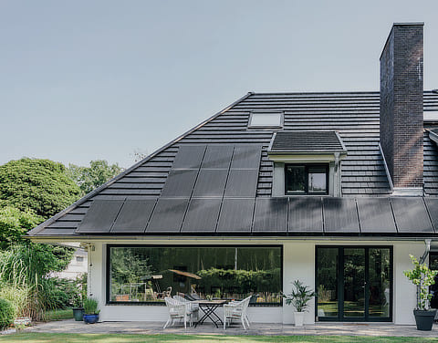 Ein schwarzes Hausdach mit integrierter Photovoltaikanlage im Vordergrund und grüne Bäume im Hintergrund.